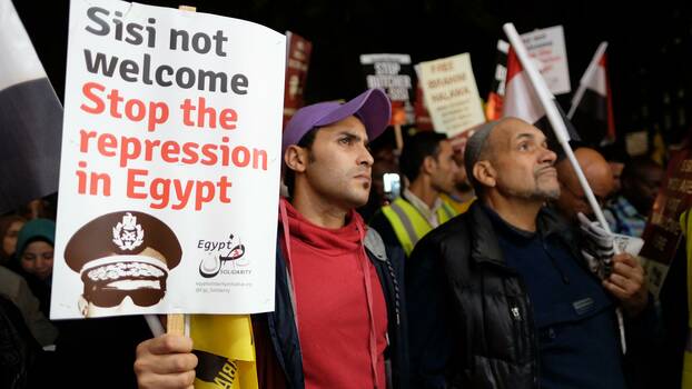 Menschen stehen mit Schildern und demonstrieren. Auf dem Schild im Vordergrund steht "Sisi not welcome. Stop the repression in Egypt".