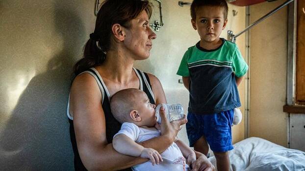 Eine Frau mit zwei kleinen Kindern aus der Region Donezk sitzt in einem Evakuierungszug auf der Flucht vor vorrückenden russischen Truppen, 6. August 2022.