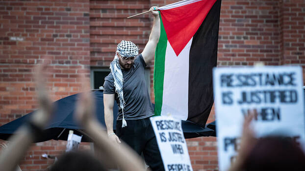 Ein Demonstrant mit einer Kufiya schwenkt die palästinensische Flagge.