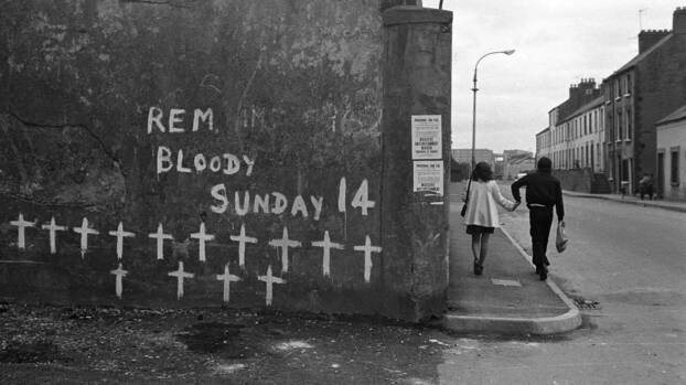 Straßenszene im nordirischen Londonderry. In Erinnerung an die Opfer des «Bloody Sunday» 1972 haben Unbekannte mit weiß 14 Kreuze an eine Mauer gemalt. Darüber steht ebenfalls in weiß: REM Bloody Sunday. Auf dem Bürgersteig rechts der Mauer läuft ein junges Päärchen Hand in Hand. . 