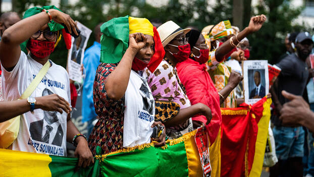 Frauen demonstrieren mit erhobenen Fäusten und halten eine große Fahne Malis.