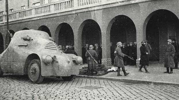Panzer vor einem Wiener Gemeindebau. Im Hintergrund sind Gefangene und beschlagnahmte Waffen des Republikanischen Schutzbundes zu sehen. Aufgenommen vermutlich am 13. Februar 1934.