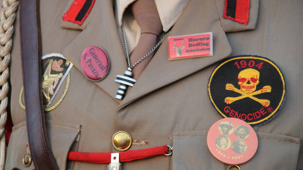 Eine Uniform mit verschiedenen Abzeichen/Symbolen, die an die Ermordung der Herero durch die deutschen Kolonialherren erinneren. 