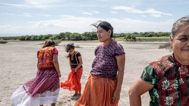 Vier zapotekische Frauen unterschiedlichen Alters (drei Generationen) stehen am Strand. Sie tragen traditionelle Kleidung (bunte Bluse und langer weiter Rock)