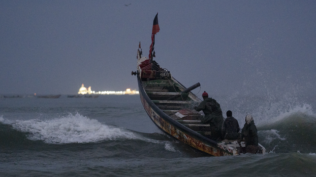 Vor der Küste von Saint Louis, Senegal, Januar 2023: Fischer auf einem traditionellen Boot, der Piroge. Am Horizont ist ein Offshore-Gas-Terminal zu sehen.