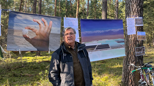 Der Umweltaktivist steht im Wald in Grünheide in Brandenburg vor einem Bild der Atacama-Wüste in Chile. 