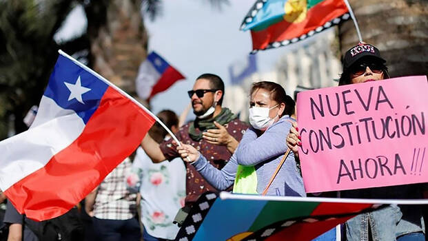 Menschen in Chile protestieren und schwenken Fahnen. Sie fordern eine neue Verfassung.