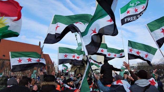 [Translate to en:] Syrische Aktivist*innen demonstrieren am 7. Jahrestag der Revolution im März 2018 in Berlin. Sie schwenken die syrische Fahne.