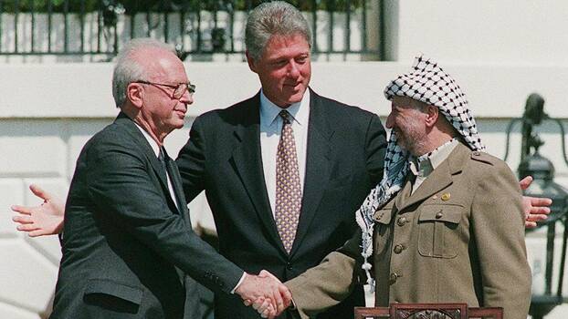 Yasser Arafat and Yitzhak Rabin shaking hands in front of Bill Clinton.