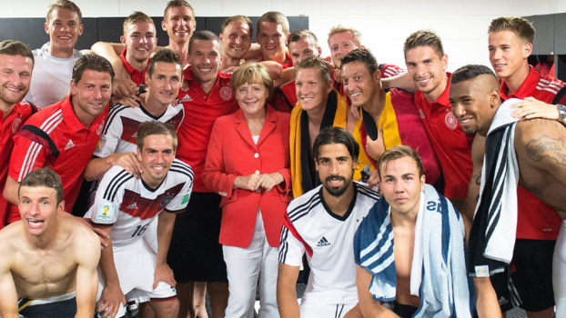 Frau (Angela Merkel) im Kreise vieler Männer (deutsche Nationalmannschaft) in einer Umkleide