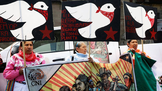 Demonstration im Mai 2023 am zocalo in Mexiko-Stadt. Mitglieder der zapatistischen Bewegung fordern die Regierung auf etwas gegen die zunehmende Gewalt gegen die indigenen Gemeinschaften in Chiapas zu unternehmen. Sie halten Schilder mit gemalten Friedenstauben mit rotem Halstuch in die Luft. 