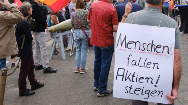 [Translate to en:] Ein Demonstrant mit einem Schild auf dem Rücken, auf dem steht "Menschen falle, Aktien steigen"