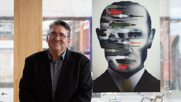 Brian Stauffer stands in front of one of his paintings. It shows a portrait of Putin with tanks, missiles and machine guns sticking out of it.
