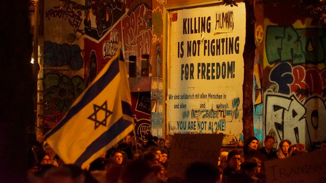 Auf dem Wandplakat wurde in der Aussage "Killing Jews ist not fighting for Freedom" das Wort "Jews" mit "Humans" überklebt. Davor ein Demonstrationszug mit israelischer Flagge.