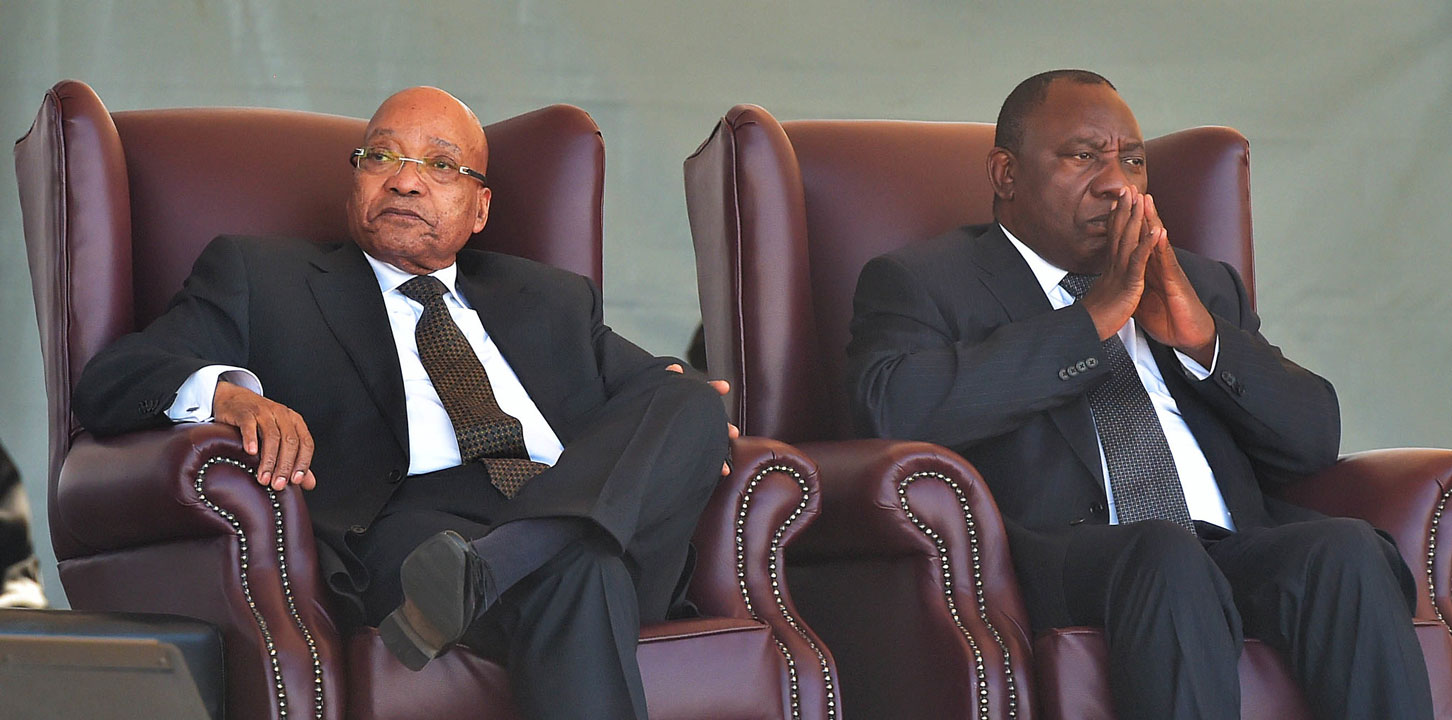 Jacob Zuma und Cyril Ramaphosa, beide im schwarzen Anzug mit Krawatte sitzen in zwei Ledersesseln nebeneinander.